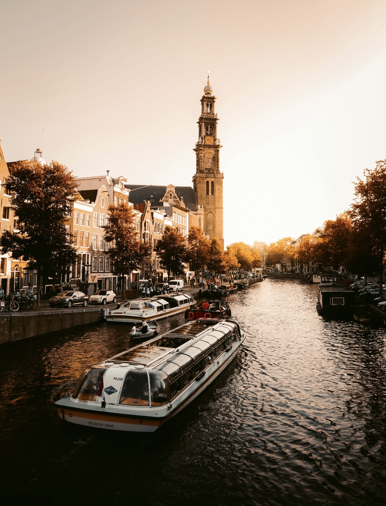 Canal de Amsterdã banhado pela luz dourada, com barcos e arquitetura da cidade