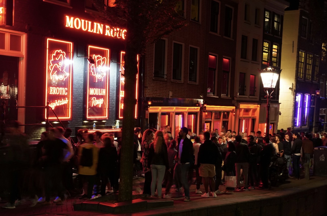 Rua de Amsterdã à noite com pessoas caminhando e fachadas iluminadas